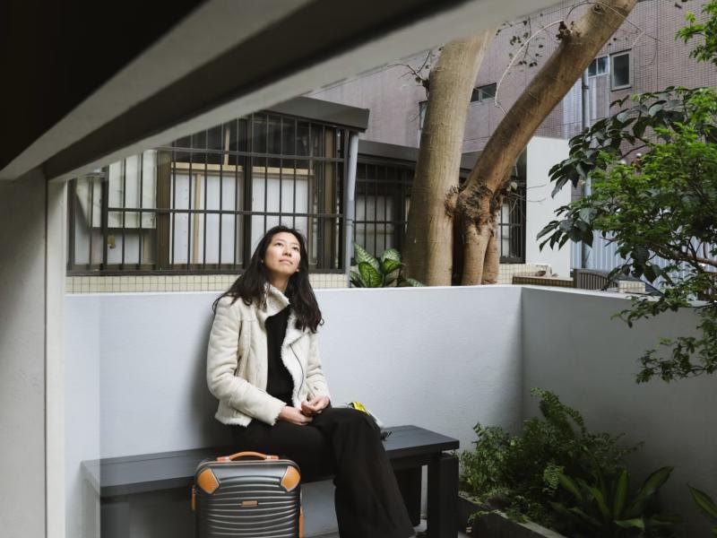 A woman sitting on a bench beside her suitcase, looking up
