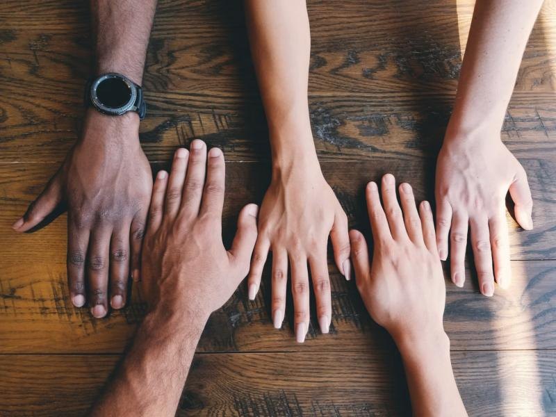 Hands of people with different skin tones resting together on a table
