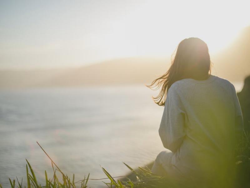 A woman sitting by the sea in soft golden light